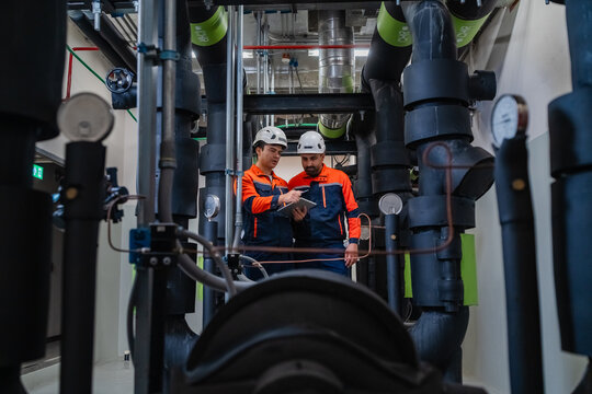 Industrial maintenance team inspecting heavy chilled water pipeline system and HVAC equipment using digital tablet for modern facility energy efficiency and smart building management.