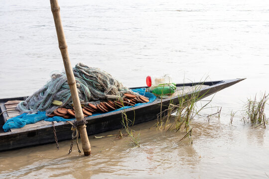 Fishing net and floats piled on a wooden boat tied to a bamboo pole in a river. Traditional freshwater fishing tackle setup in rural waters.