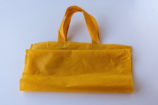 Folded yellow non woven tote bag with handle on white background. Environmentally conscious packaging product.