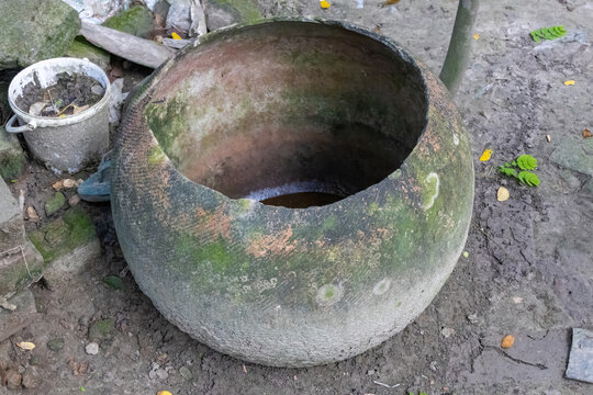 Large broken vintage earthenware vessel covered in green moss. Antique clay container on dirt ground.