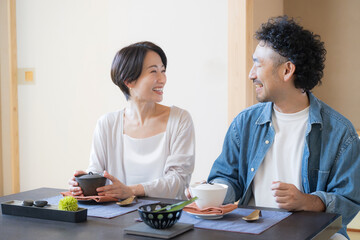 温泉旅館のような和室で座る、会話しながら旅行を楽しむ日本人夫婦の観光旅行や国内旅行の宿泊先イメージ © kapinon