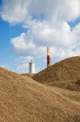 Massive piles of gravel dominate an active industrial quarry site featuring storage silos under a bright blue sky with cumulus clouds. © Grey Zone