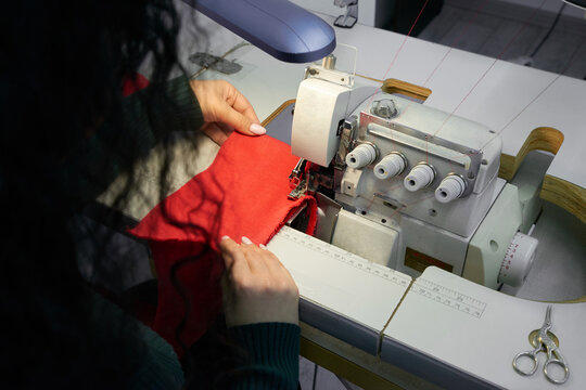 Young woman using professional overlock sewing machine in workshop studio. Equipment for edging, hemming or seaming clothes at tailors shop