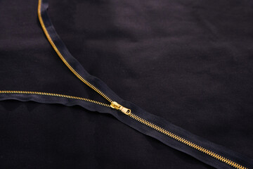 Open golden zipper on black fabric, tailor background © Maria