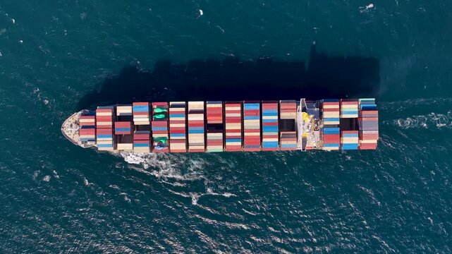 A topdown aerial shot of a massive freighter vessel loaded with colorful shipping containers navigating through deep blue sea water, illustrating global trade and logistics.