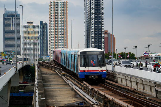 BTS Skytrain moves along an elevated railway through Bangkok, with office towers and multilane roads nearby in a busy urban setting, Thailand, Bangkok, April 26, 2026.