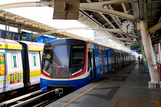 BTS Skytrain at an elevated Bangkok station beneath a large roof, with a platform clock and city buildings beyond in a busy urban setting, Thailand, Bangkok, April 26, 2026.