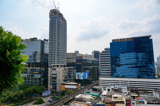 Modern glass office towers and shopping buildings rise above an elevated railway in central Bangkok in a busy urban setting, Thailand, Bangkok, April 26, 2026.