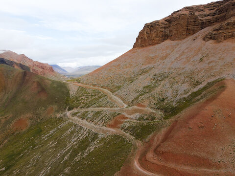Aerial view of a winding switchback dirt road ascending a steep mountain slope beneath a rocky bluff