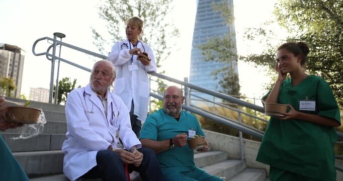 Diverse group of doctors and nurses eating and talking together on stairs outside the hospital. Healthcare professionals enjoying a well deserved rest, fostering teamwork and camaraderie outdoors