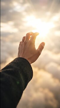 Hand reaching toward bright sun above clouds. Reaching for sunlight. Hope, aspiration and possibility concept. Human connection with nature.