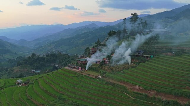 Stunning aerial view of a remote village with smoke rising from houses during sunset over the mu cang chai rice paddies in vietnam