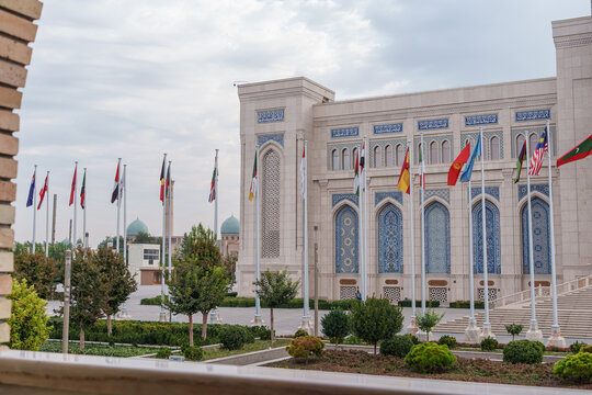 Ornate government building with arched windows, national flags, landscaped grounds, and domed architecture beneath a cloudy sky in Dushanbe, Tajikistan