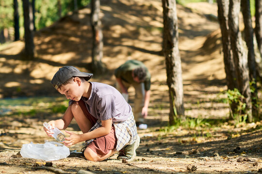 Caucasian child boy collecting glass bottle litter in forest during cleanup activity with father. Image suitable for environmental campaigns and volunteering promotion
