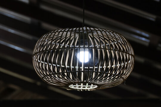 Woven metal pendant light glowing against dark industrial ceiling, creating dramatic interior atmosphere with reflective detail and modern decorative design