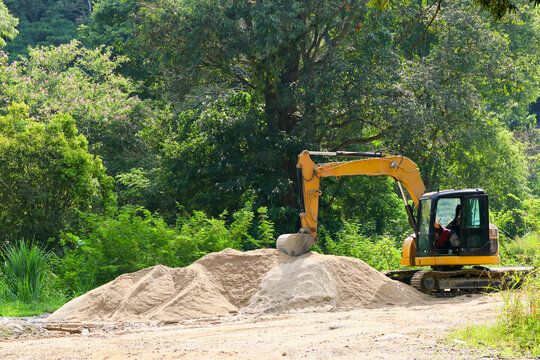 Yellow excavator beside sand pile in lush forest construction site