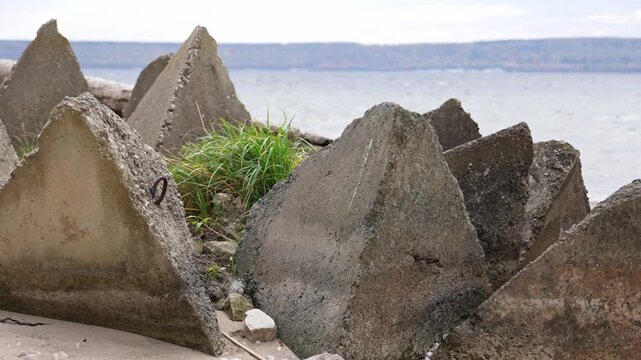 Weathered stone pyramids sit silently near the shoreline where soft waves gently touch the sandy ground and small patches of green grass grow between the sturdy relics of a bygone defensive era