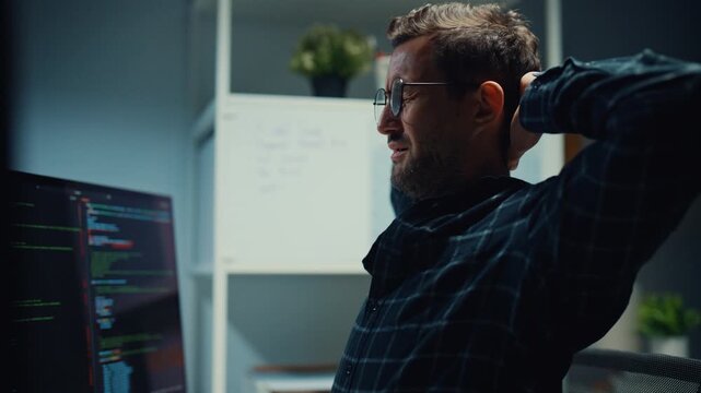 Tired male developer stretches arms to release stress from heavy workload in office at night. Employee burnout relief and recovery, Workplace health care, Rested mind for better productivity concept.