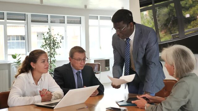 Aggressive african businessman expressing his discontent to colleagues sitting around table with upset look 