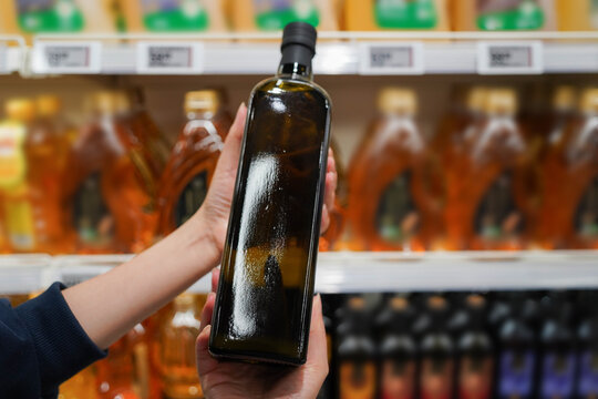 Woman choosing cooking oil in the supermarket. Close up of hand holding bottle of oil at store.