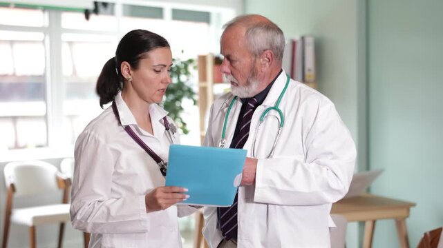 Elderly male and adult female physicians holding paper folder with test results and discussing patient cases 