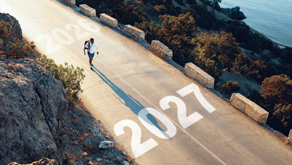 Naklejka premium Man walking on road with years 2026 and 2027 marked on the surface near a coastline in a natural setting