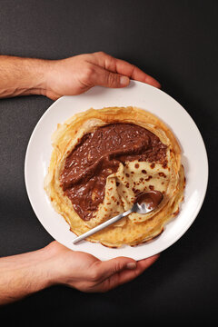 Hands holding plate of crepes with chocolate hazelnut spread