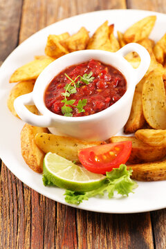 Tomato salsa dip bowl with crispy potato wedges on white plate