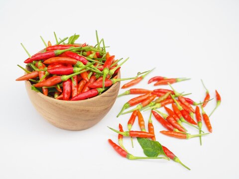 Several ripe red bird's eye chilies are in a wooden cup set on a white surface; I grew these chilies naturally myself.