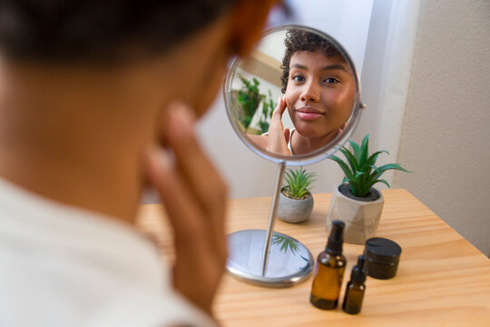 Young African American woman applying facial moisturizer looking