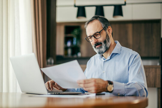 Mature man analyzing documents and working on laptop
