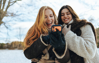 Women laugh at a smartphone outdoors in winter