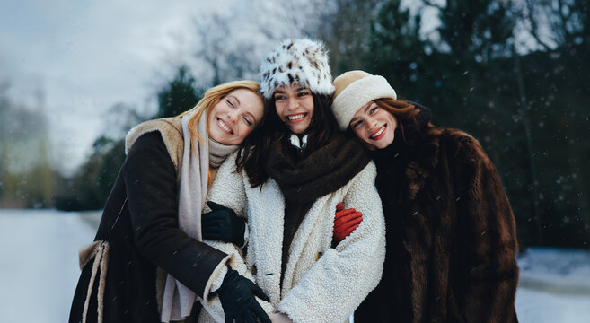 Women friends hug together in snow during winter