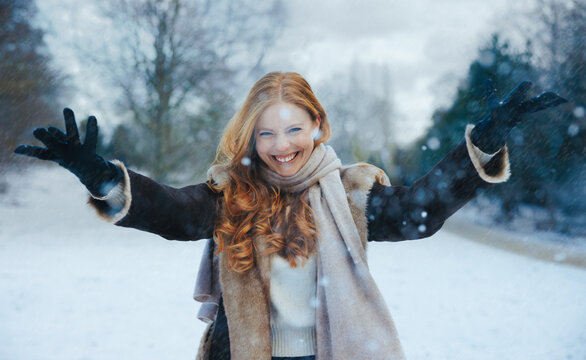 Woman welcomes falling snow with open arms outdoors
