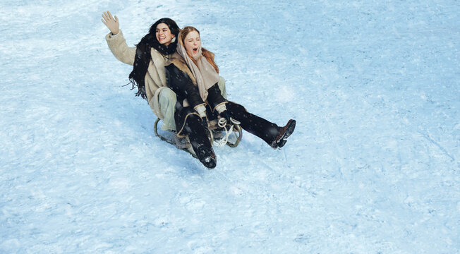 Sled carries women downhill through winter snow