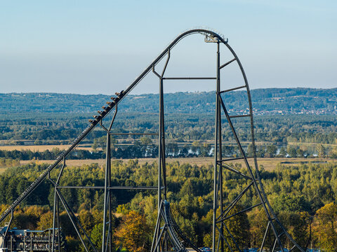 Roller coaster descending a steep track at an amusement park in Poland, with excited people experiencing an intense thrill ride, funfair attractions and adrenaline filled entertainment.