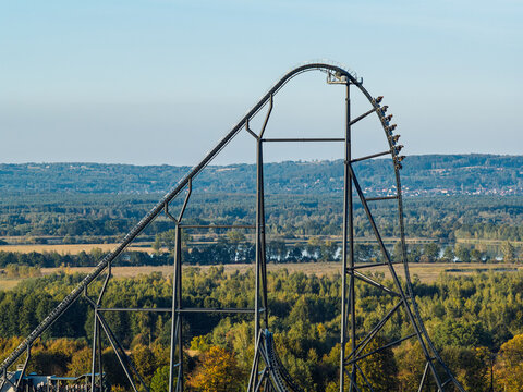 Roller coaster descending a steep track at an amusement park in Poland, with excited people experiencing an intense thrill ride, funfair attractions and adrenaline filled entertainment.