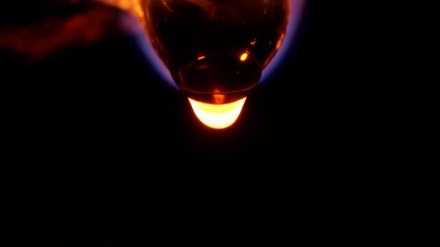 Glowing molten material stretches and retracts beneath a rounded form with blue flame-like light against a black background in abstract fluid motion footage