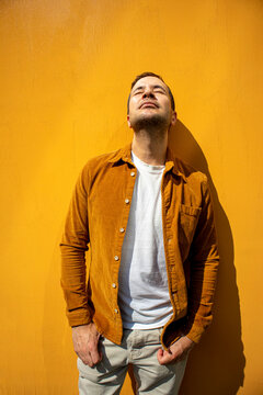 A relaxed man enjoys warm sunlight outdoors against a yellow wall