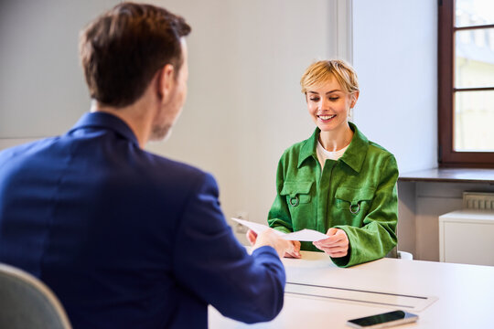 Smiling woman hands a document to a recruiter at the office