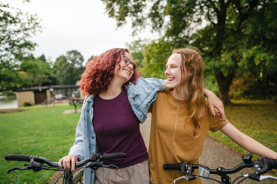Smiling teenage friends walk bicycles and talk in an urban park