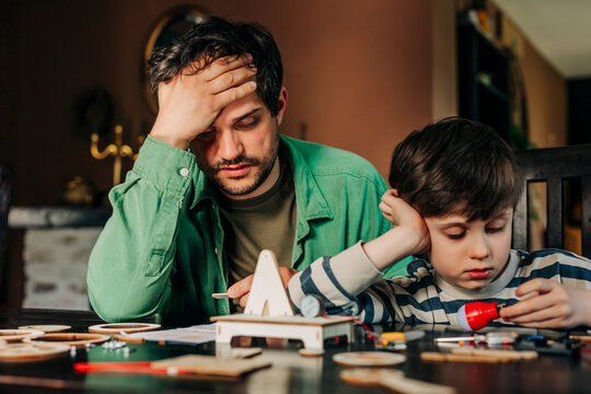 Frustrated father and son assembling wooden construction kit at home