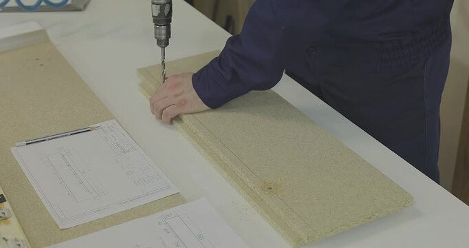 A craftsman assembles wooden furniture in a workshop, following technical drawings. A furniture maker or furniture designer assembles wooden furniture parts on a workbench 
