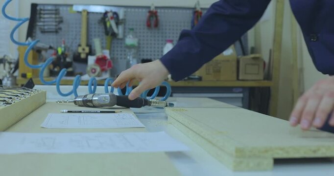 A furniture maker or furniture designer in blue workwear marking and preparing particle board parts on a workbench in a furniture factory workshop.