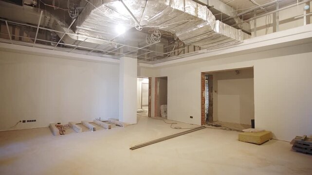 Open room displays exposed ceiling ductwork and raw wall openings. Active construction environment shows major office overhaul process