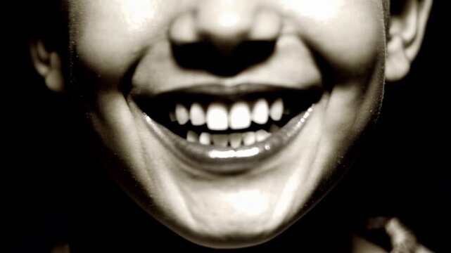 Close up of smiling person showing teeth as lips move in changing expression, high contrast monochrome portrait against a dark background