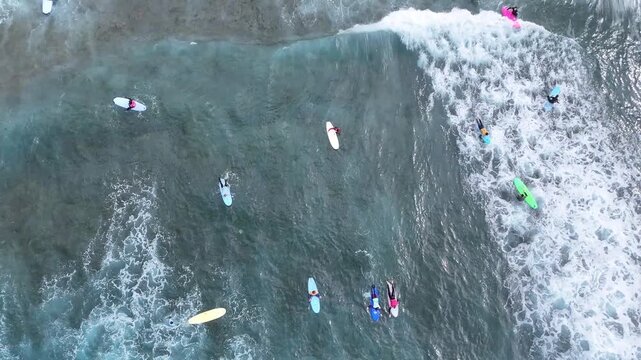 Aerial view of surfers riding waves in the ocean. Multiple unrecognizable people on surfboards navigating through the water, with dynamic wave patterns and foamy surf visible in the background