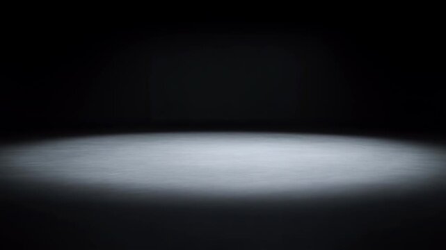 Soft white spotlight gradually expands across an empty dark stage. Theater title cards, event introductions, and presentation openings.