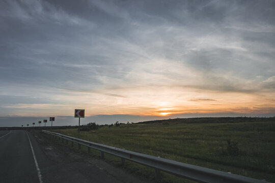 Roadside landscape; sunset on a warm summer evening with an asphalt highway stretching into the distance; cloudy evening weather in the Kazakh steppe
