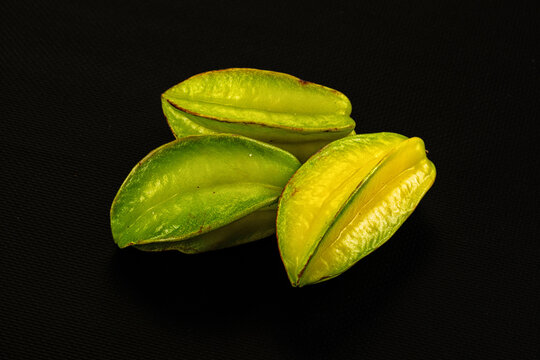 Black matte surface, three yellow and green carambola star fruit, tropical fruit arrangement